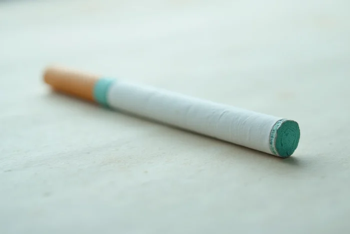 Macro d'une cigarette slim avec filtre coloré teal sur fond papier texturé, détail du taux de goudron et de la couleur du filtre Vogue